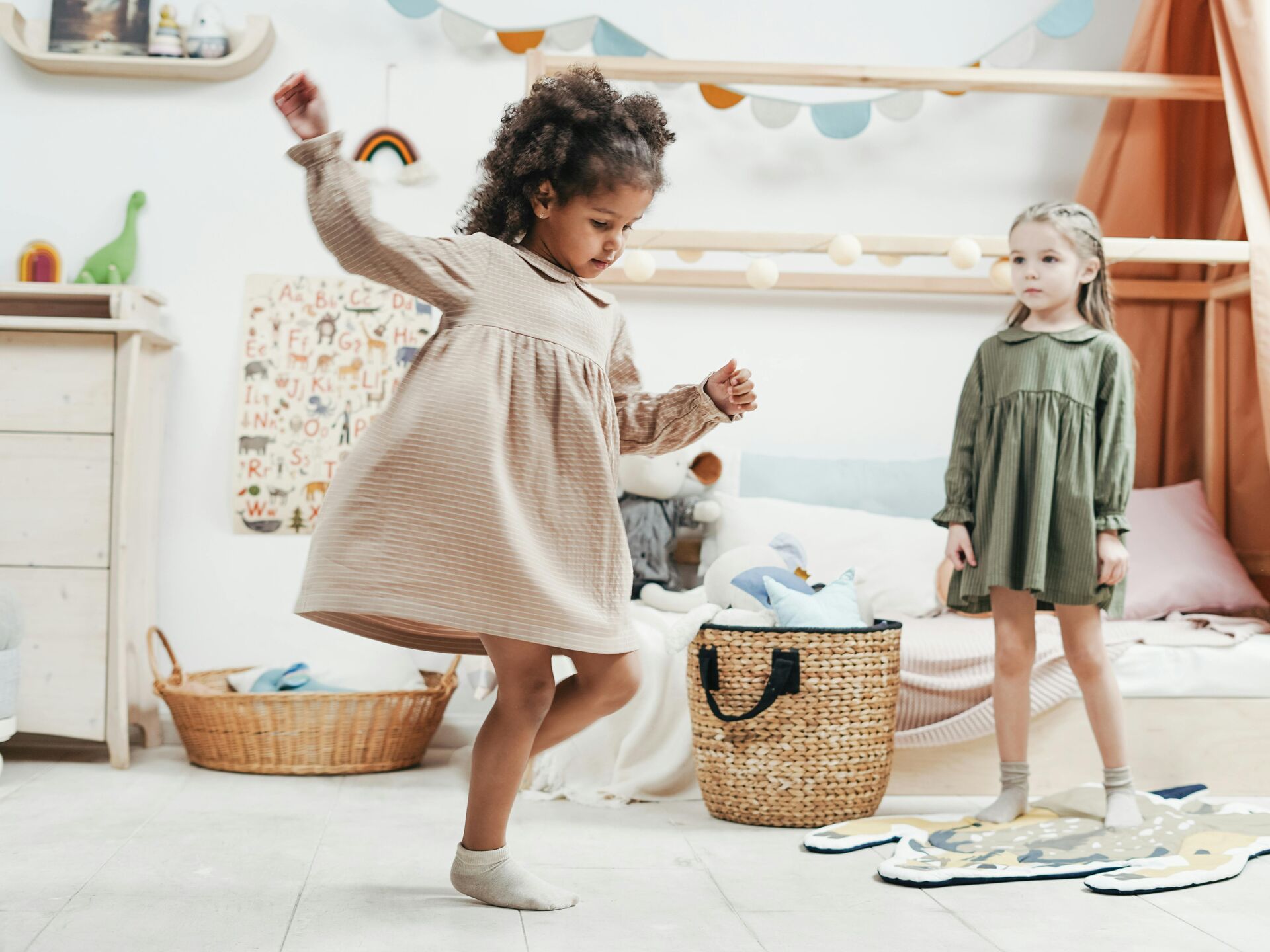 Ein Kind tanzt fröhlich in einem hell eingerichteten Kinderzimmer, während ein weiteres Kind im Hintergrund steht und zusieht.