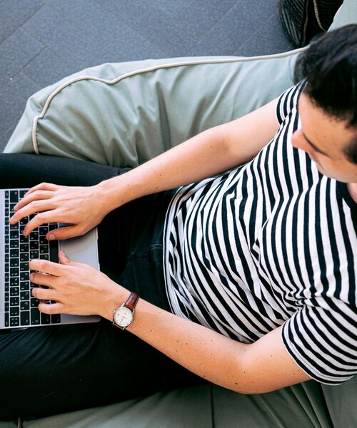 Person sitzt entspannt auf einem Sitzsack und arbeitet am Laptop.